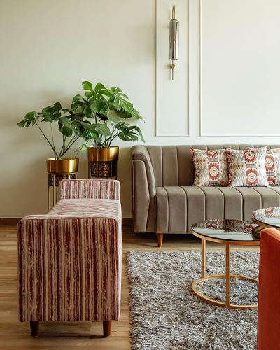Living room with taupe channel-tufted sofa, striped bench, brass planters and round glass coffee table on a shag rug