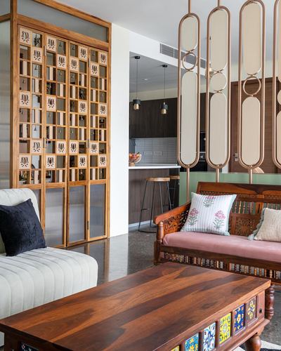 Living room with carved wooden bench, jali cabinet, tiled coffee table, and hanging capsule dividers