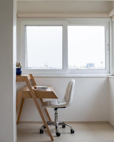 Small nook with angled wooden desk, white chair, and window overlooking city skyline