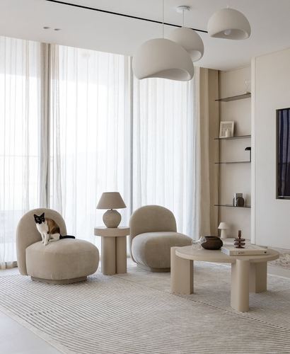 Beige living room with curved velvet chairs, dome pendants, and a cat on a chair