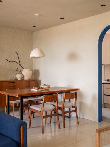 Dining area with wooden table, textured plaster wall, and blue archway leading to kitchen