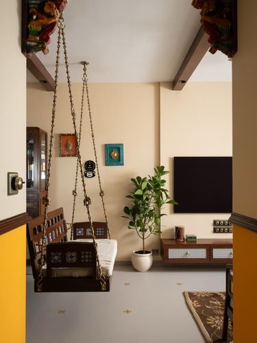 Wooden brass-chained swing hangs in doorway of Indian living room with tiled console and plant
