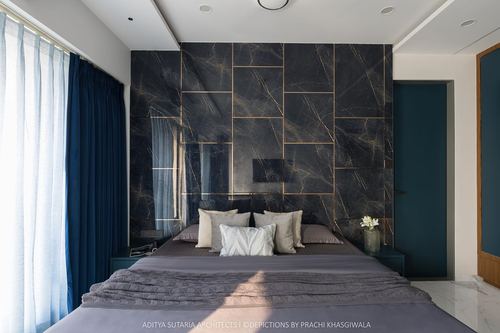 Bedroom with dark stone panelled headboard wall, brass inlay lines and navy curtains