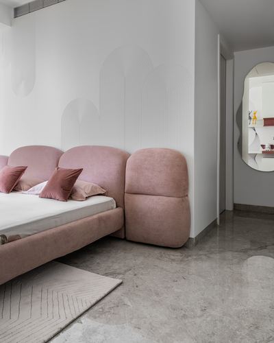 Blush velvet scalloped bed against arched-line wallpaper with stone floor and round mirror beyond