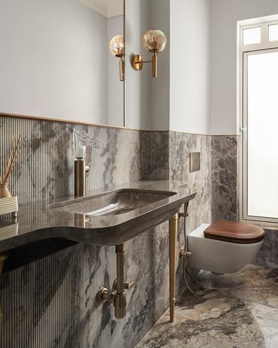 Bathroom with sculptural stone vanity, brass fixtures, fluted stone wall, wall-hung toilet with wood seat
