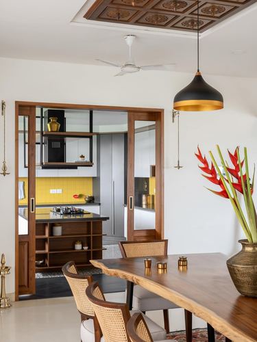 Dining area with live-edge wood table, cane chairs, and view through wooden sliding doors into a yellow-tiled kitchen