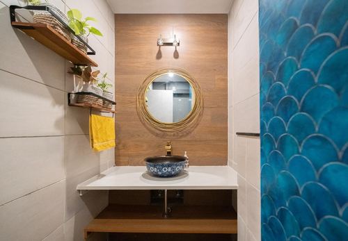 Bathroom with round mirror, patterned vessel sink, wood wall and scalloped teal tile shower wall