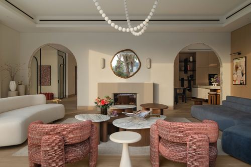 Living room with curved sofa, red patterned chairs, marble tables, and arched doorways either side of a fireplace