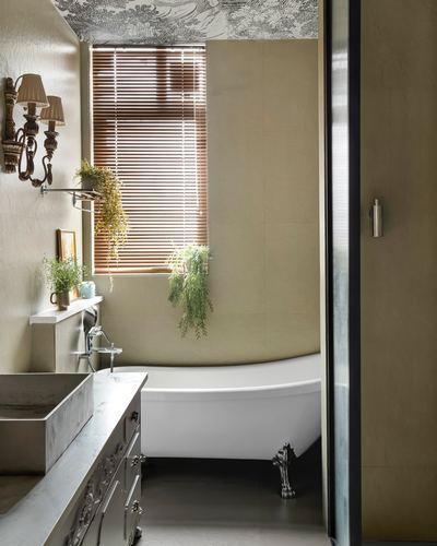Freestanding clawfoot tub beneath window with hanging plants and marble vanity in eclectic bathroom