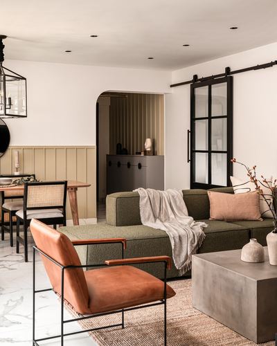 Living room with olive boucle sectional, leather armchair, and black-framed glass sliding door