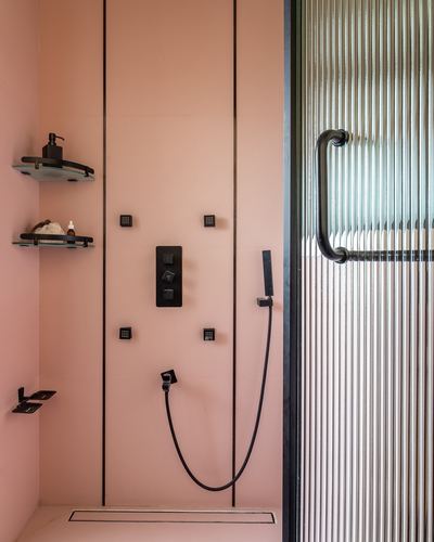 Pink-tiled shower stall with black fixtures beside a fluted glass door