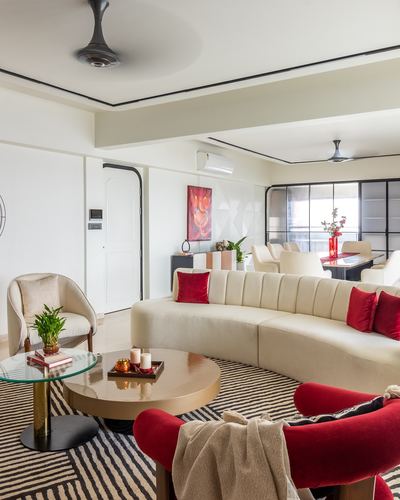 Curved cream sofa with red cushions beside round brass coffee tables on a striped rug