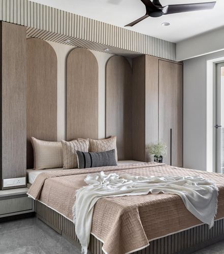 Bedroom with arched wood-panelled headboard wall, beige bedding, and built-in wardrobe beside window