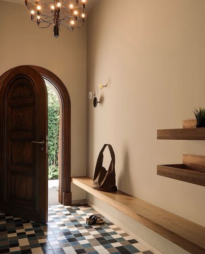 Arched wooden door opens to greenery beside patterned tile floor and floating wood shelves in entryway