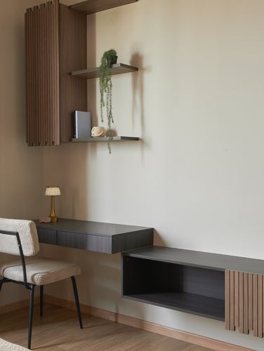 Wall-mounted study desk with dark cabinetry, wood shelf with trailing plant, cane chair, fluted wood panel storage