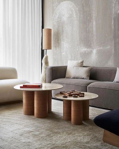 Grey sofa with textured plaster wall and two round stone-top tables with cylindrical wood bases