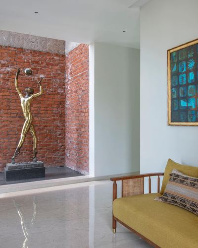 Foyer with bronze dancer sculpture in brick niche, framed art, and mustard cane settee