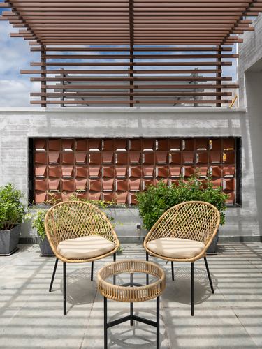 Rooftop terrace with cane chairs, wood pergola, and a terracotta jali screen wall