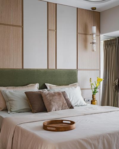 Bedroom with olive headboard, wood paneled wall, and layered pendant light above nightstand.
