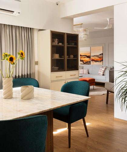 Dining table with teal velvet chairs and marble top, opening into living room with art panels