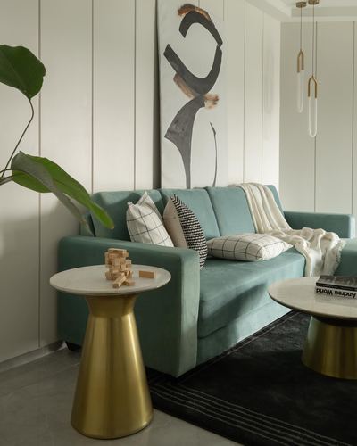 Teal velvet sofa with patterned cushions beside brass-and-marble side tables and abstract art