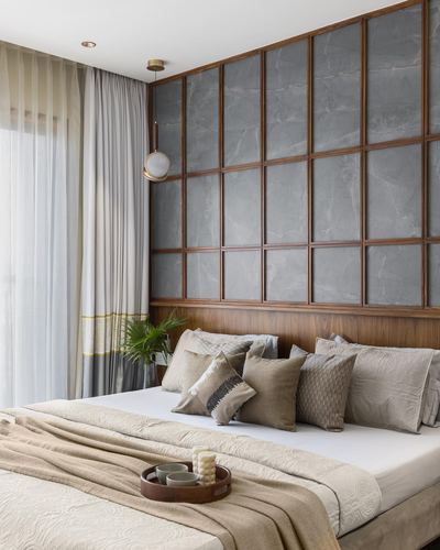 Bedroom with grid-paneled stone and wood headboard wall, layered neutral cushions, sheer curtains