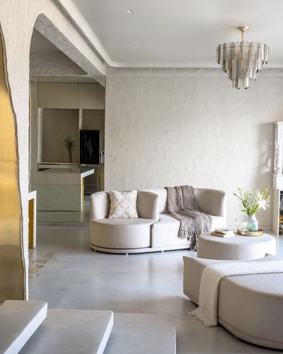 Curved beige sofa under tiered chandelier beside sculpted plaster archway in Mumbai penthouse living room