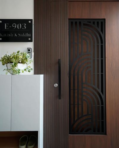 Entrance door with fluted wood paneling, black art deco grille, nameplate and potted plant