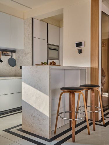 Kitchen with marble waterfall island, two wooden bar stools, and white cabinetry under natural light