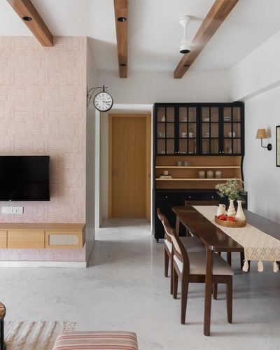 Dining and living area with patterned pink wall, black glass hutch, and wood beam ceiling
