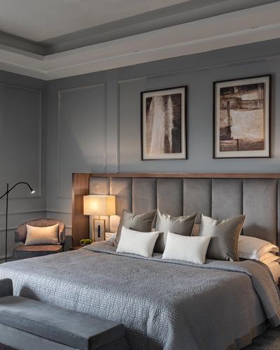 Grey upholstered king bed with tall wood-trimmed headboard beneath two abstract framed artworks