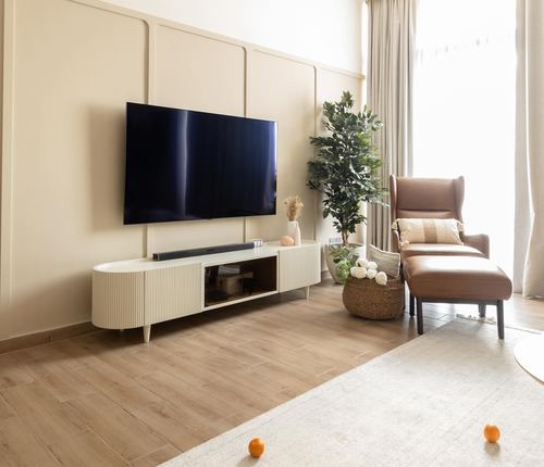Living room with fluted cream TV console, wall-mounted TV, and tan leather wingback chair by window