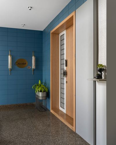 Entrance foyer with blue tiled wall, wood-framed door, brass sconces, and terrazzo flooring