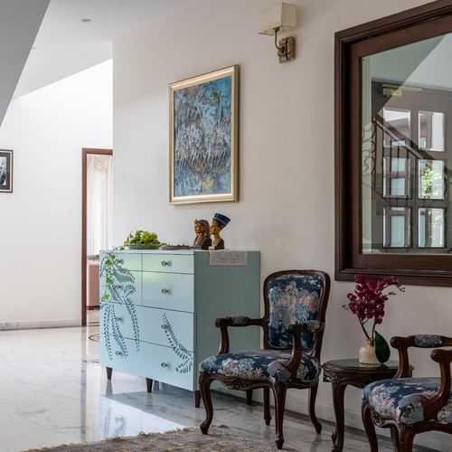 Foyer with painted blue chest, framed artwork, carved mirror and floral upholstered chairs