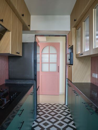 Galley kitchen with wood cabinetry, black countertops, diamond tile floor, and an arched pink door beyond