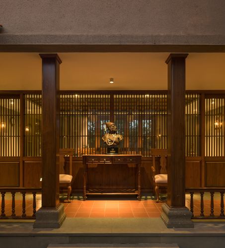 Symmetrical veranda with teak columns framing a console table with a bronze bust, terracotta floor