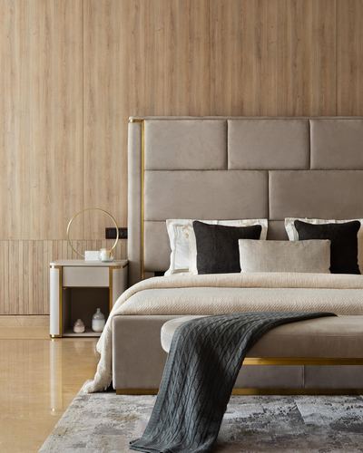 Beige upholstered bed with brass trim against wood-paneled wall, nightstand with ring decor beside it