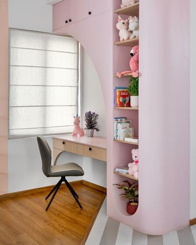 Pink curved wall study nook with wood desk, shelves of stuffed toys, and window seat area