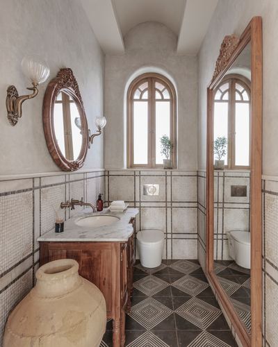 Goan bathroom with carved oval mirror, marble-top wooden vanity, arched window and mosaic tile walls