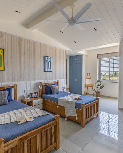 Twin teak beds with blue linens in a kids bedroom with striped wallpaper and sloped ceiling