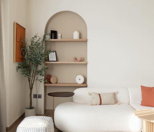 Living room corner with arched niche shelves, olive tree, and white boucle sofa