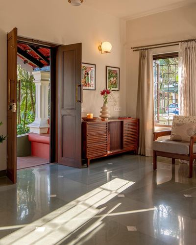 Sunlit entryway with open wooden door, terrazzo floor, wooden console and armchair, view to garden