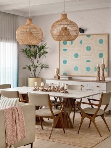 Dining area with two rattan pendant lights over a marble-top table with sculpted wood base, teal artwork on wall