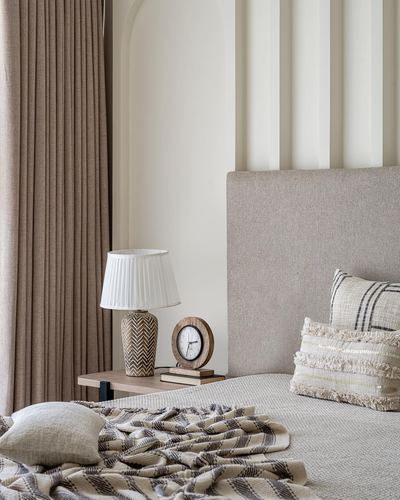 Beige upholstered bed with textured pillows beside a fluted wall and wooden nightstand