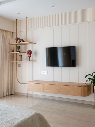 Bedroom wall with fluted paneling, wall-mounted tv, floating wood credenza, and hanging brass display shelf