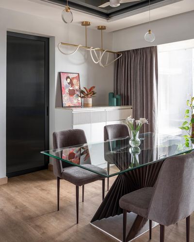 Dining area with glass table on sculptural base, grey velvet chairs, and sideboard with art