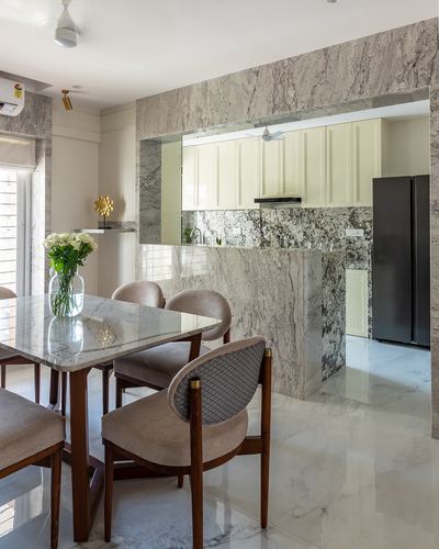 Dining table with marble top and cane-back chairs facing an open marble-framed kitchen