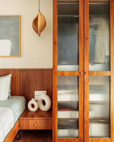 Bedroom corner with wooden fluted wardrobe, ribbed panel headboard, and sculptural pendant light