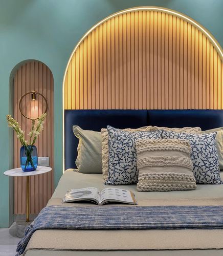 Bed with navy velvet base and fluted wood arched headboard, patterned pillows, marble side table with vase against seafoam green wall