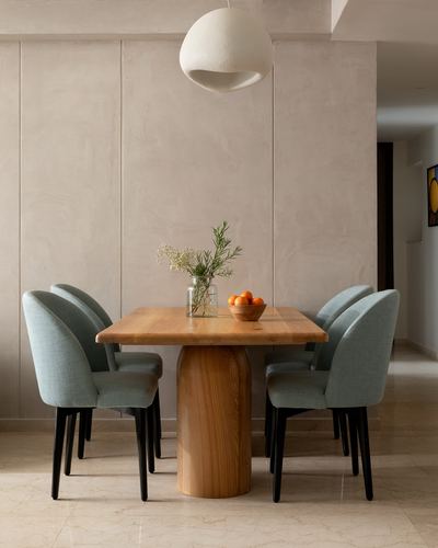 Wooden dining table with sage chairs beneath a round pendant light against a plaster wall